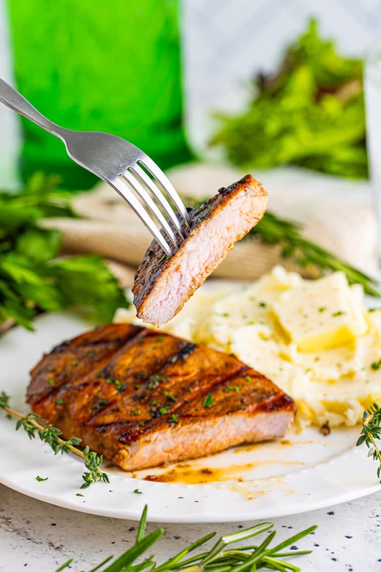 A grilled balsamic marinated pork chop sliced to show the juicy interior, served with mashed potatoes.