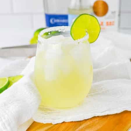 A classic margarita in a stemless glass with a salted rim and a fresh lime wheel