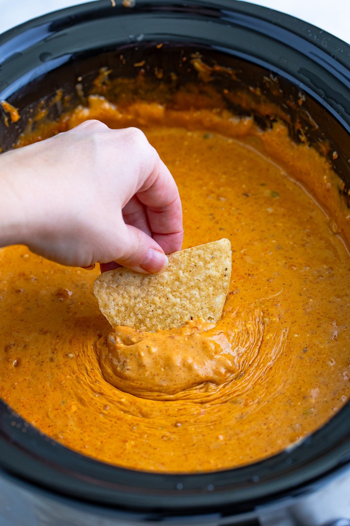 Crock Pot Queso Dip in slow cooker with a hand dipping a chip into it