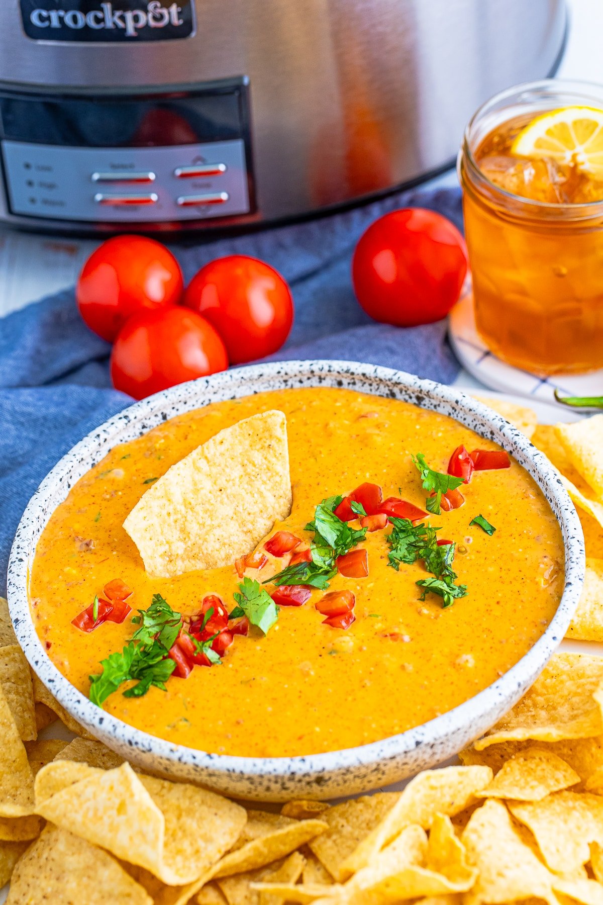 cilantro and tomatoes on top of Crock Pot Queso Dip served in a bowl with chips