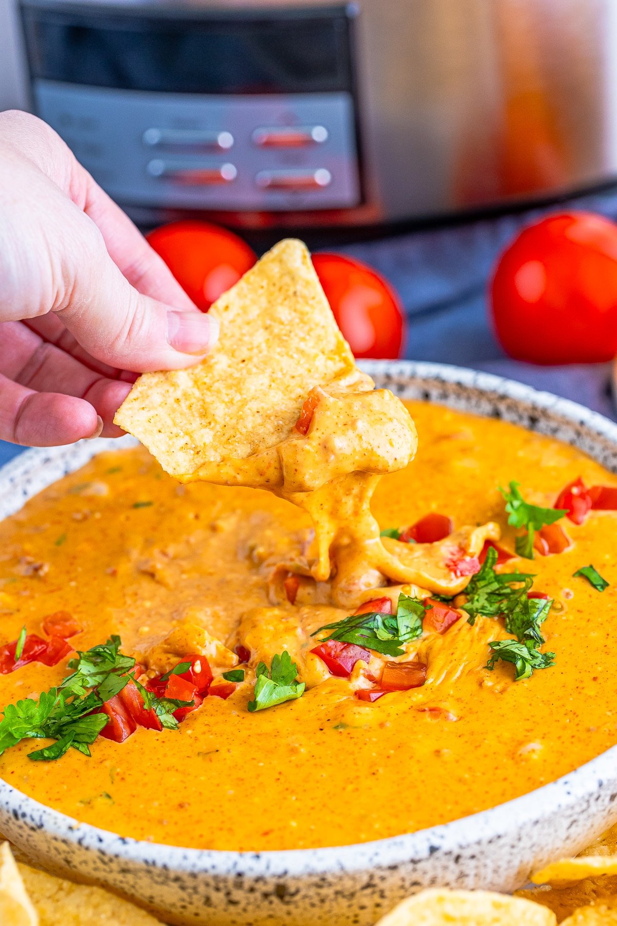 a hand holding a chip in air that has been dipped in Crock Pot Queso Dip