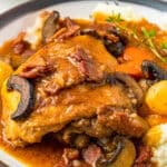 A serving of coq au vin with a braised chicken thigh, mushrooms, and pearl onions over mashed potatoes