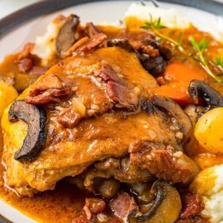 A serving of coq au vin with a braised chicken thigh, mushrooms, and pearl onions over mashed potatoes