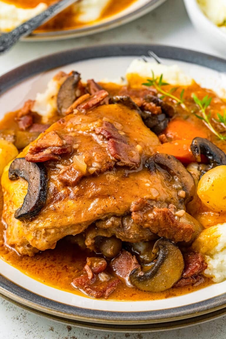 A serving of coq au vin with a braised chicken thigh, mushrooms, and pearl onions over mashed potatoes