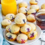 A plate of mini berry pancake bites with fresh raspberries, blueberries, and a glass of orange juice.