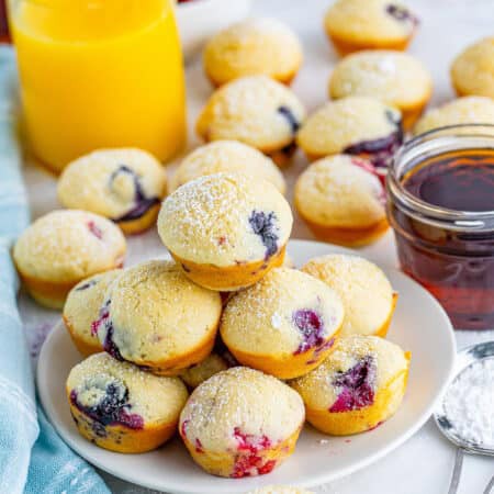 A plate of mini berry pancake bites with fresh raspberries, blueberries, and a glass of orange juice.