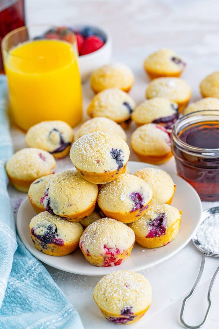 A plate of mini berry pancake bites with fresh raspberries, blueberries, and a glass of orange juice.
