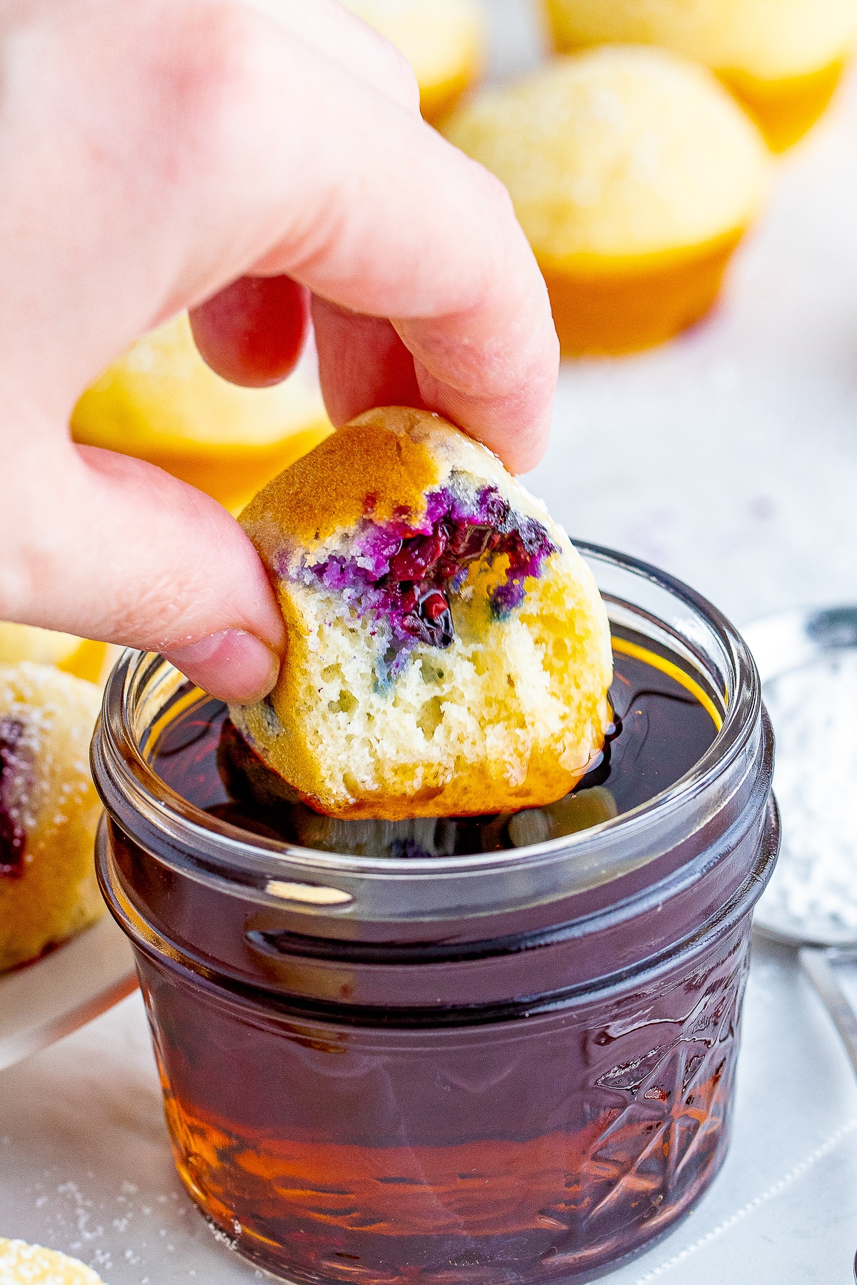 a hand dipping a Pancake Bites into maple syrup that has a bite taken out