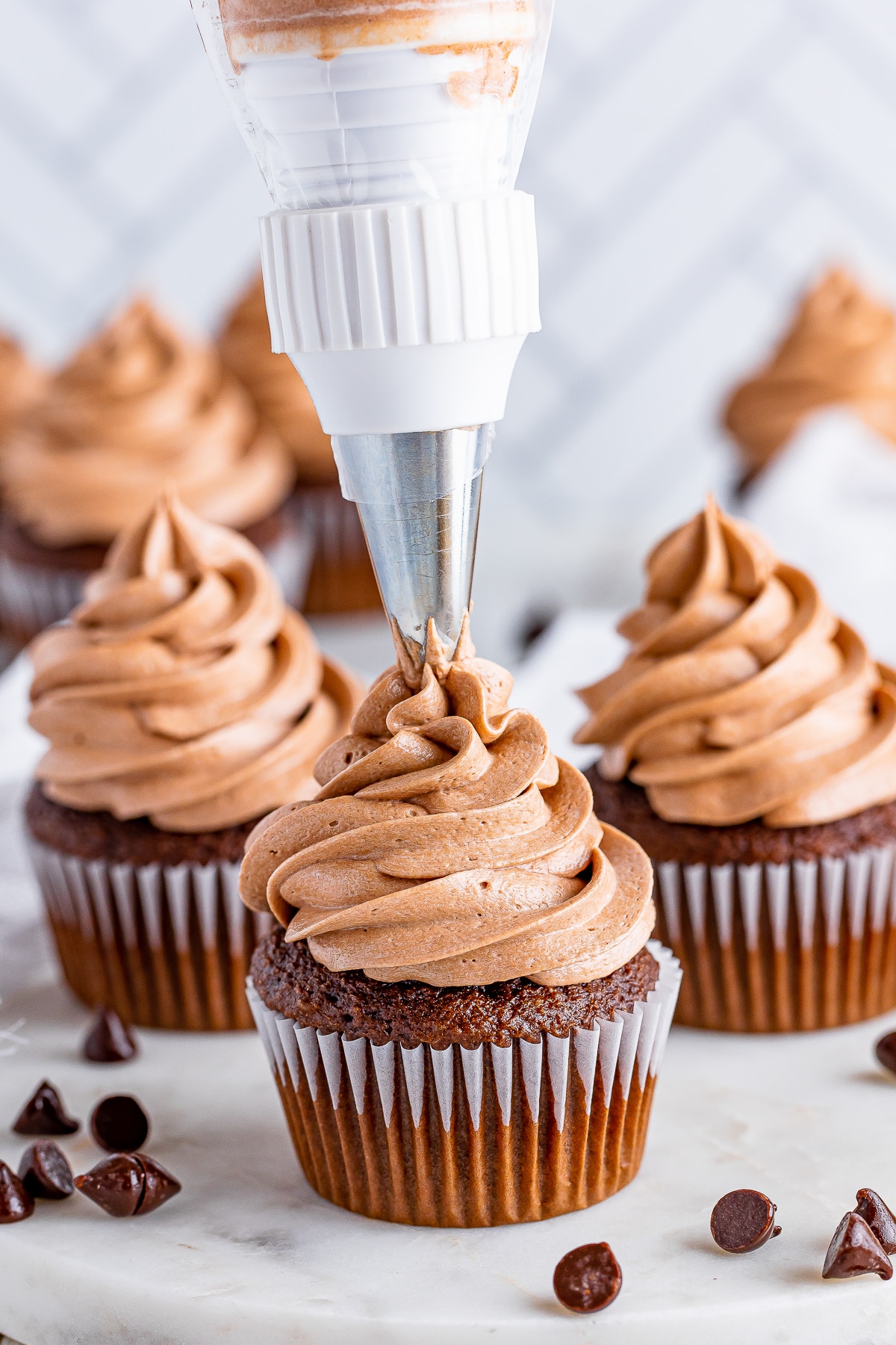 piping Chocolate Cream Cheese Frosting on top of a chocolate cupcake