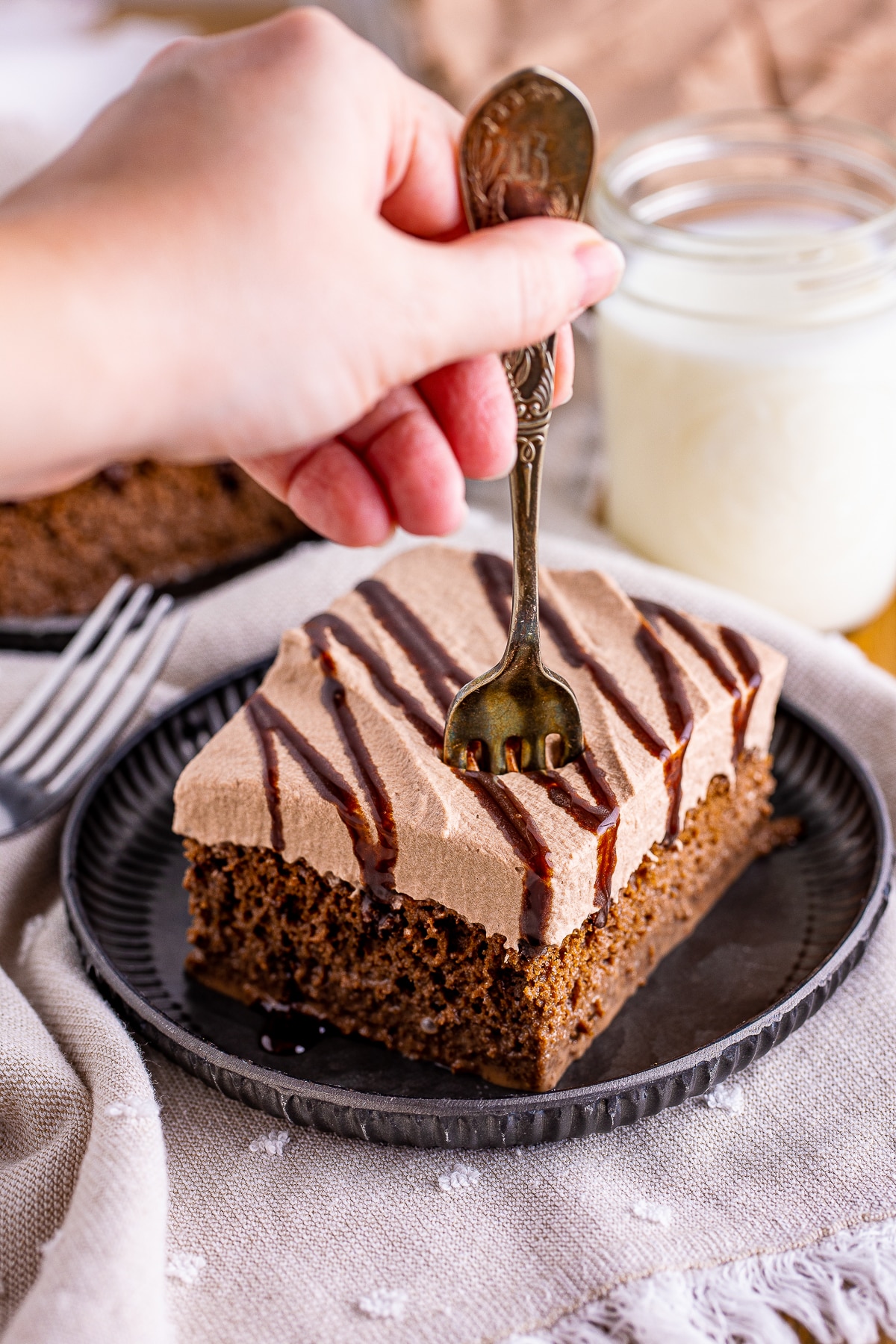 a hand holding a fork taking out a bite of chocolate tres leches cake from a slice on a plate