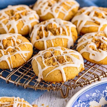 Coffee cake cookies with cinnamon crumble centers and vanilla glaze drizzle on a wire rack.