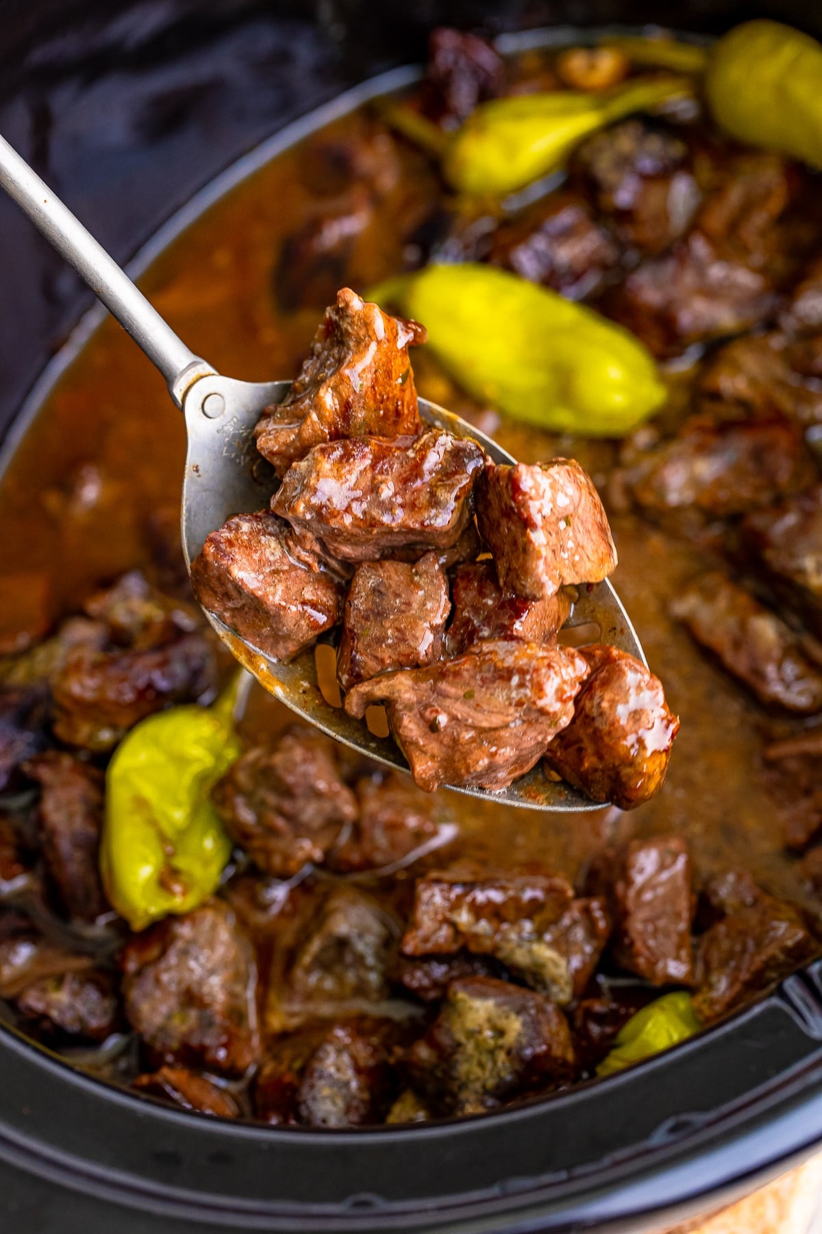 a spoon holding up Steak Bites in air over a slow cooker