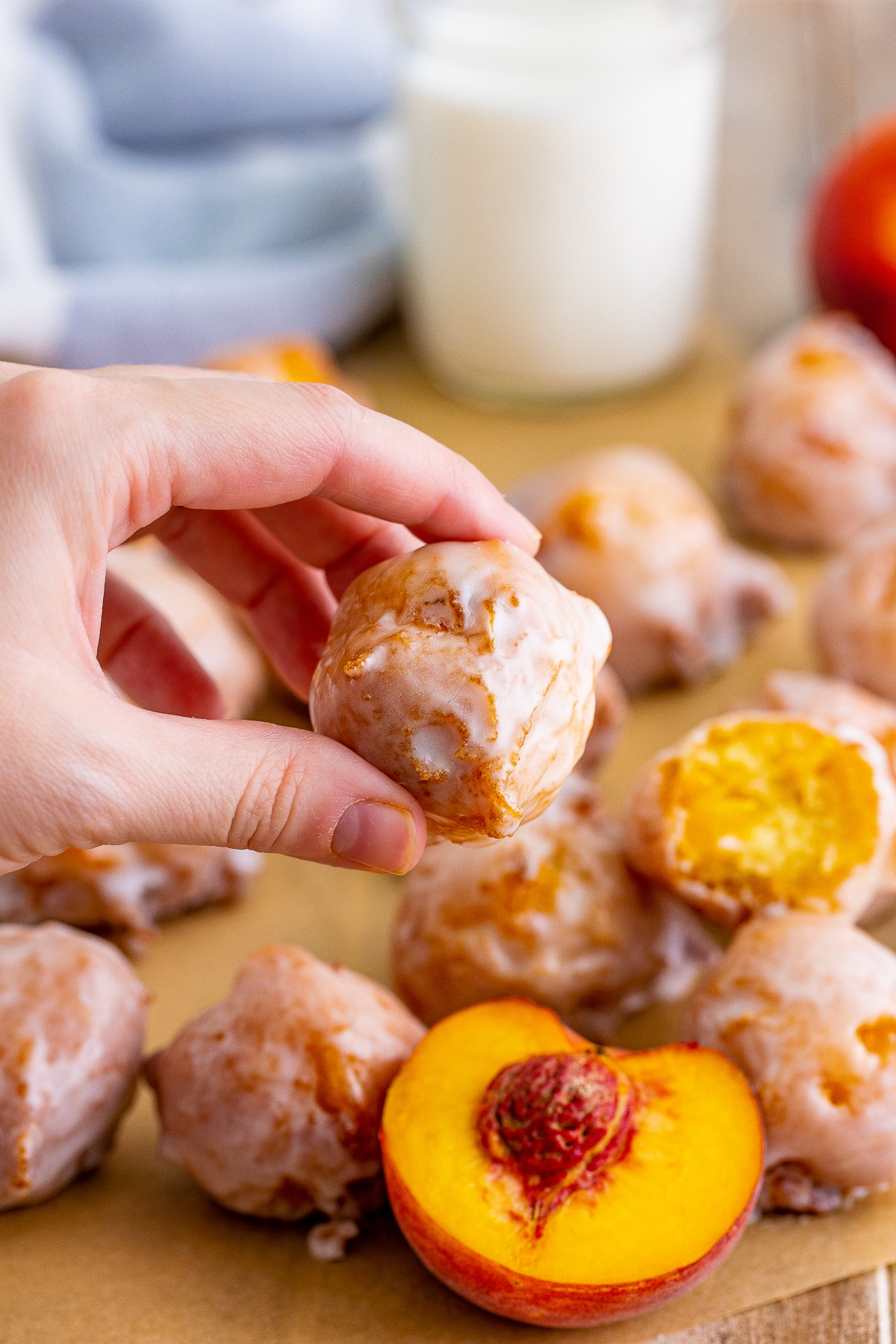 a hand holding up one Peach Fritters in air with fresh peaches