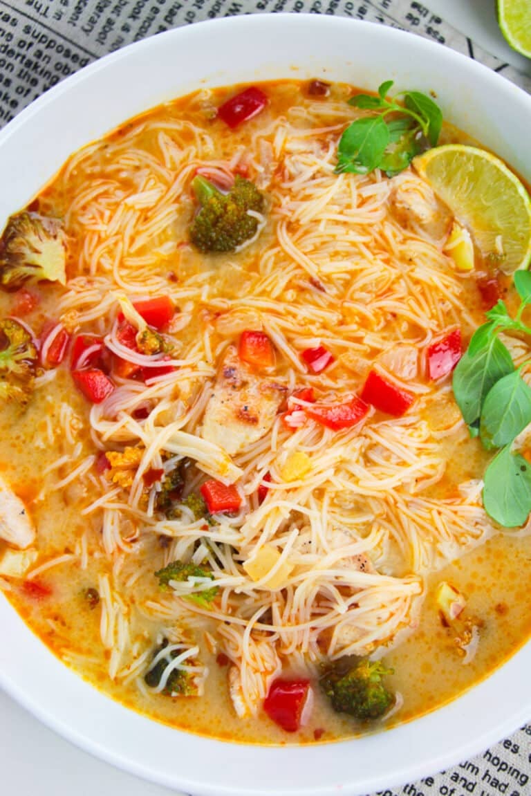 Thai Red Curry Soup in a white bowl loaded with rice noodles, chicken, broccoli, and lime.