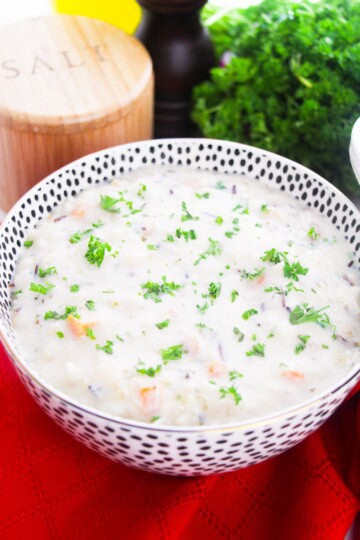 A bowl of creamy wild rice soup topped with fresh parsley on a red napkin.