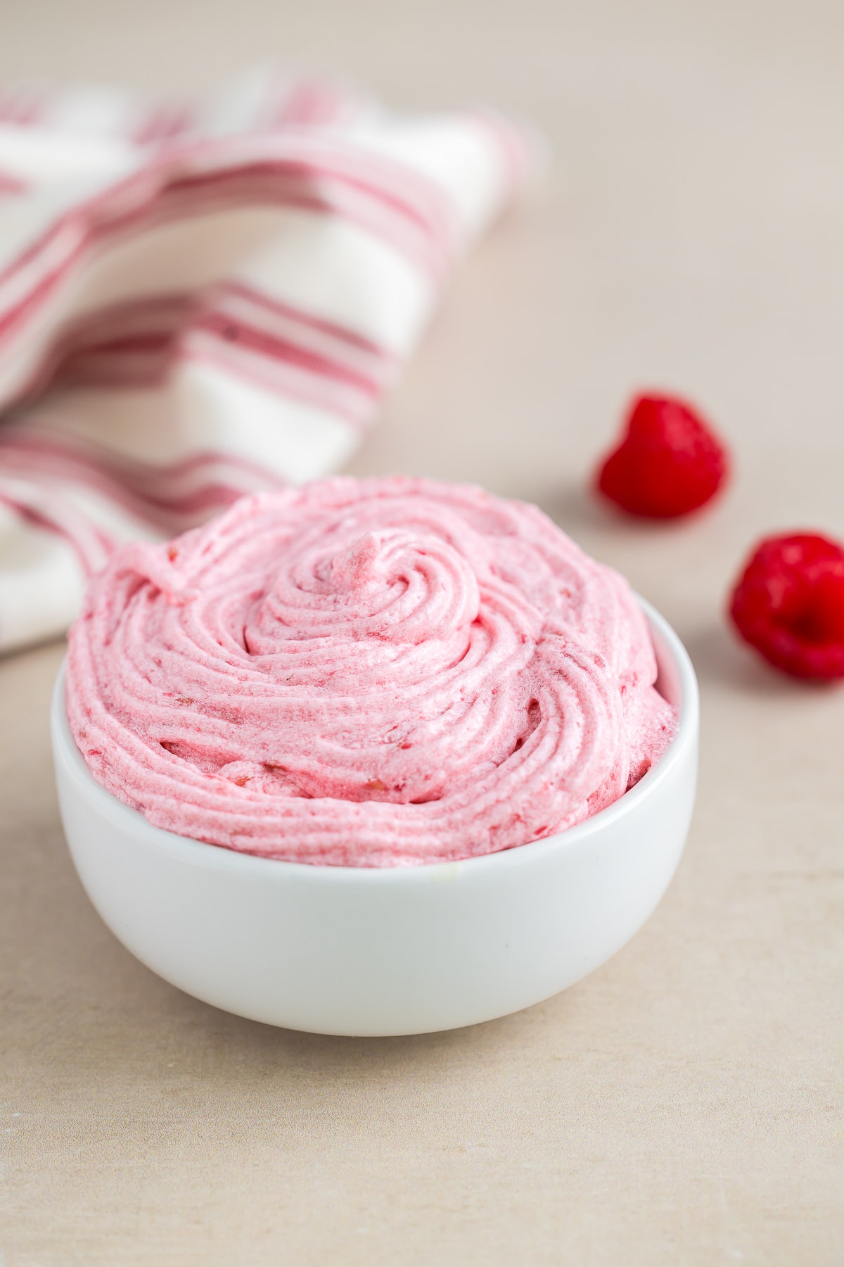 Raspberry Frosting in a small white bowl on a tan table top
