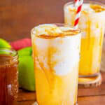 An apple cider float in a tall glass with vanilla ice cream, caramel drizzle, and a striped straw.