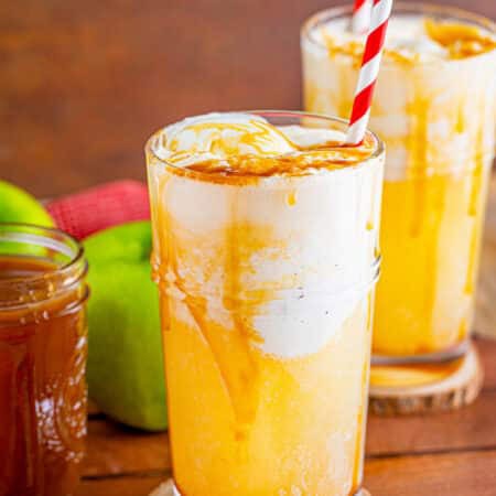 An apple cider float in a tall glass with vanilla ice cream, caramel drizzle, and a striped straw.