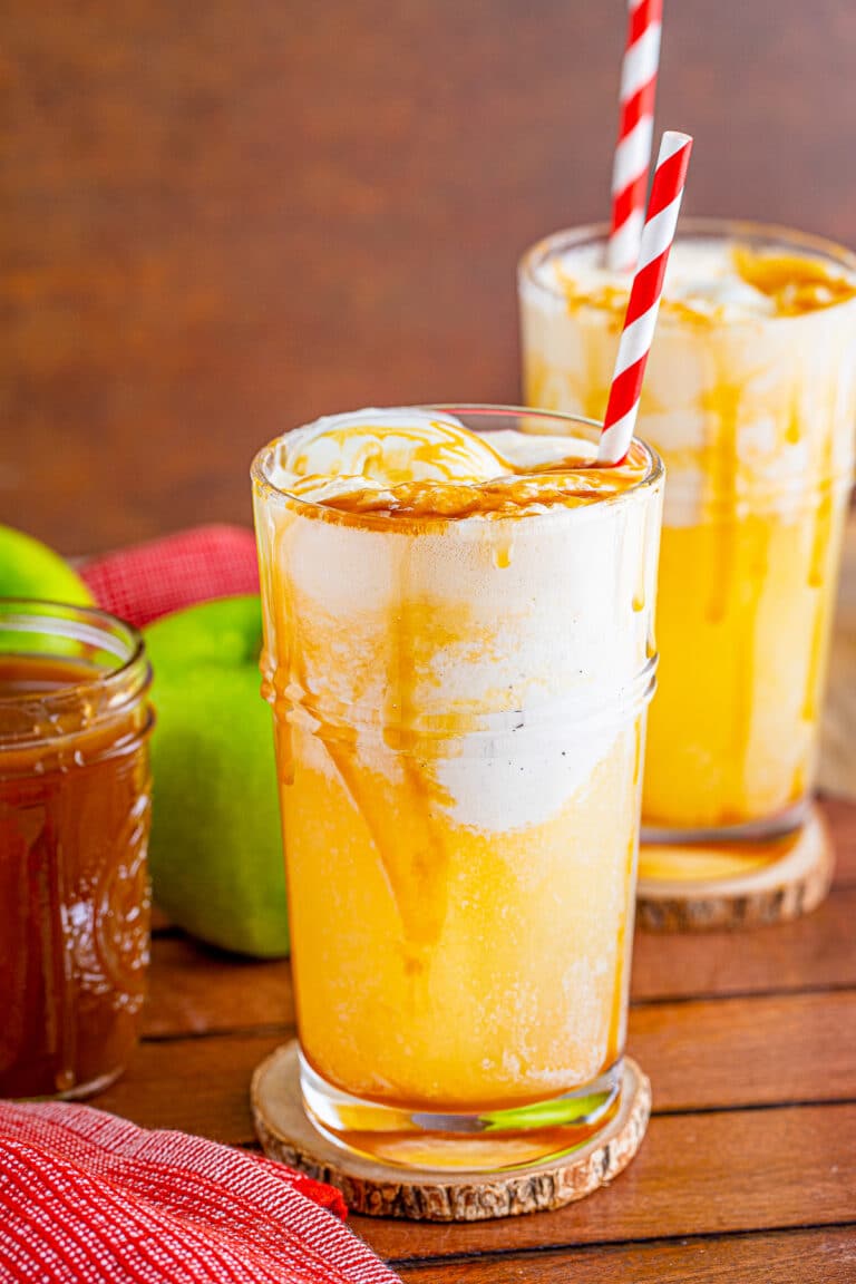 An apple cider float in a tall glass with vanilla ice cream, caramel drizzle, and a striped straw.