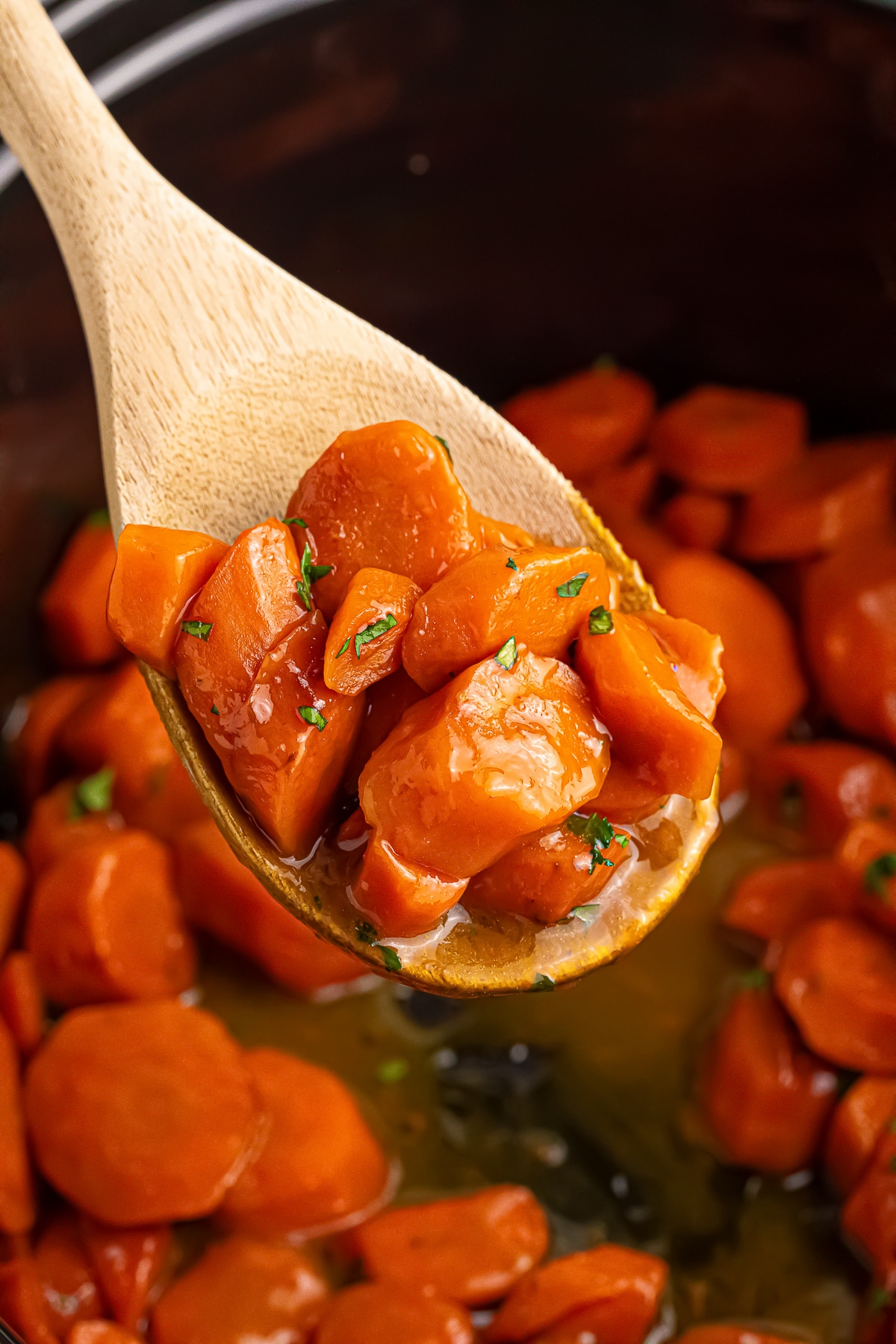 a wooden spoon holding up Maple Glazed Carrots over a slow cooker