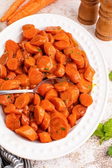 A white plate of maple glazed carrots garnished with parsley.