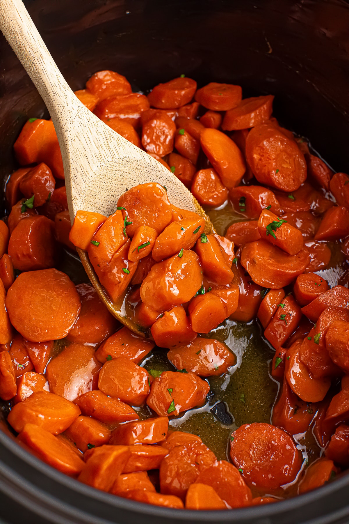 Maple Glazed Carrots in a slow cooker with wooden spoon