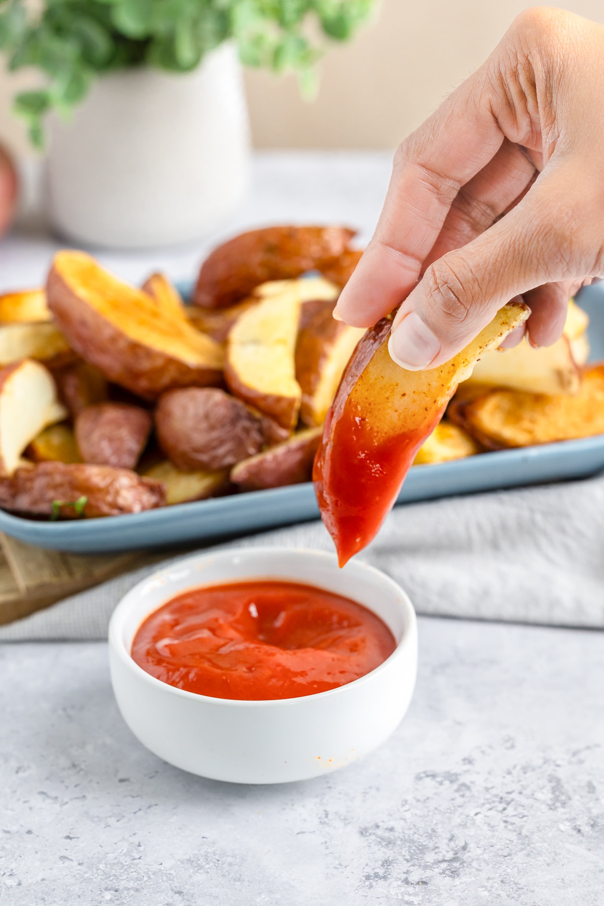 a hand holding up Crispy Potato Wedges that has been dipped in ketchup