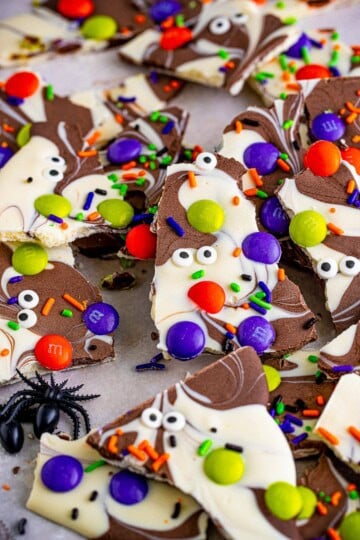 Pieces of halloween bark with swirled chocolate and white chocolate topped with M&Ms, candy eyeballs, and orange and purple sprinkles.