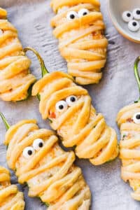Jalapeno Popper Mummies wrapped in crescent dough with candy eyes on parchment.