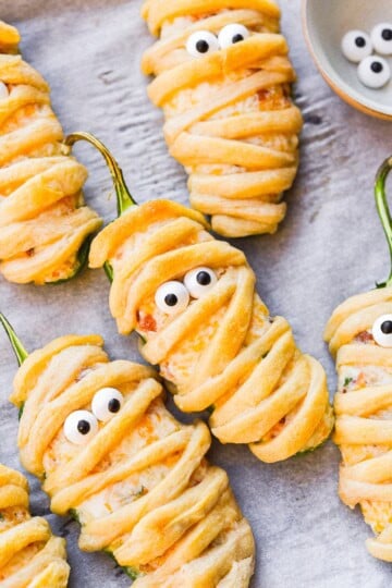 Jalapeno Popper Mummies wrapped in crescent dough with candy eyes on parchment.