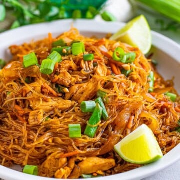 Bowl of Easy Filipino Pancit Recipe with Chicken topped with green onions and lime wedges, ready to serve.