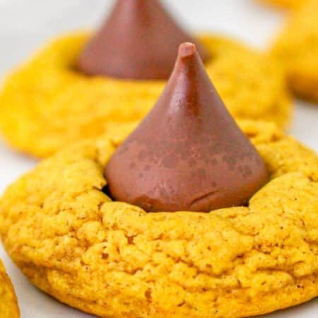 A close up of a soft pumpkin cookie with a chocolate Hershey Kiss pressed into the center on a white platter.