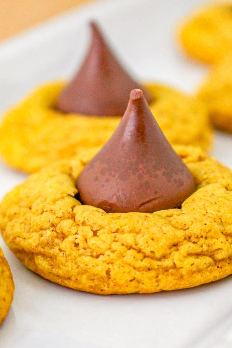 A close up of a soft pumpkin cookie with a chocolate Hershey Kiss pressed into the center on a white platter.