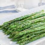 Grilled asparagus spears on a white plate with a mason jar candle and blue striped napkin