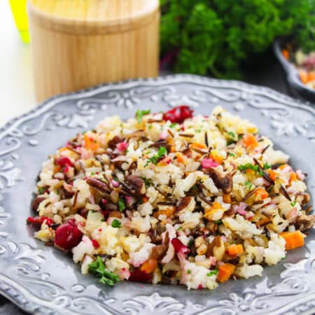 Wild Rice Pilaf with pecans and cranberries served on a gray scalloped plate with fresh parsley.