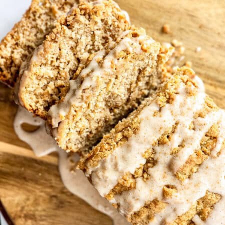 Sliced Apple Bread with crumble topping and glaze on a wooden board.