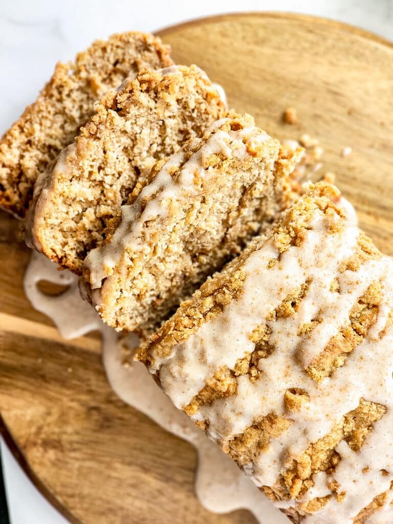 Sliced Apple Bread with crumble topping and glaze on a wooden board.