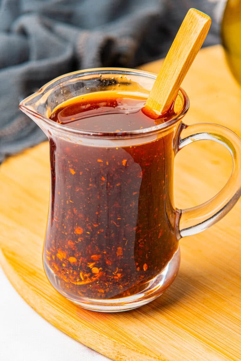A glass jar of homemade chili oil with red chili flakes settled at the bottom and a spoon
