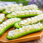 Dill cream cheese cucumber boats arranged on a wood board, piped with whipped cream cheese filling.