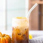 A tall glass of pumpkin cream cold brew with a glass straw and fluffy pumpkin cream layer on top.