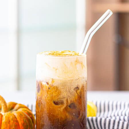 A tall glass of pumpkin cream cold brew with a glass straw and fluffy pumpkin cream layer on top.
