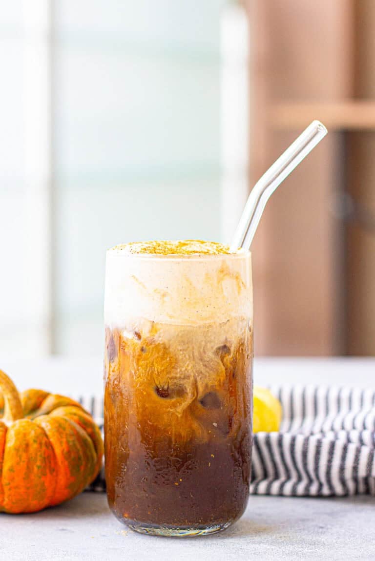 A tall glass of pumpkin cream cold brew with a glass straw and fluffy pumpkin cream layer on top.