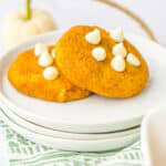 Two soft Pumpkin Snickerdoodles with white chocolate chips stacked on a white plate.