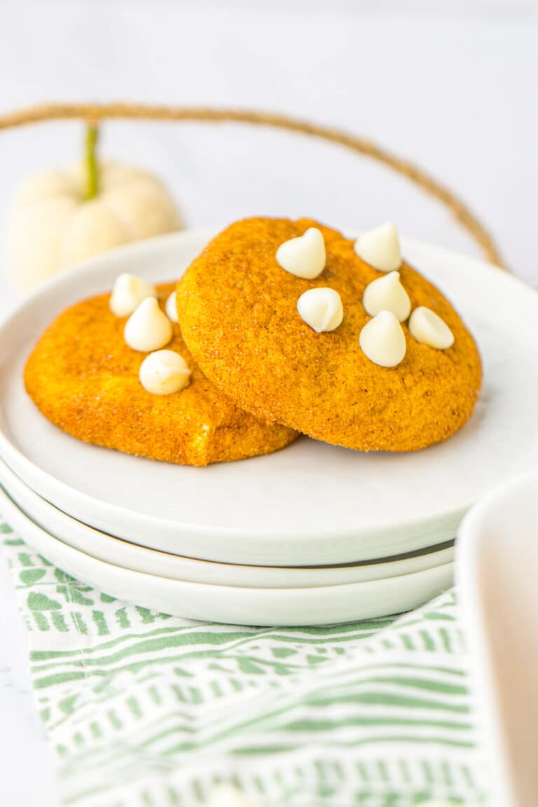 Two soft Pumpkin Snickerdoodles with white chocolate chips stacked on a white plate.