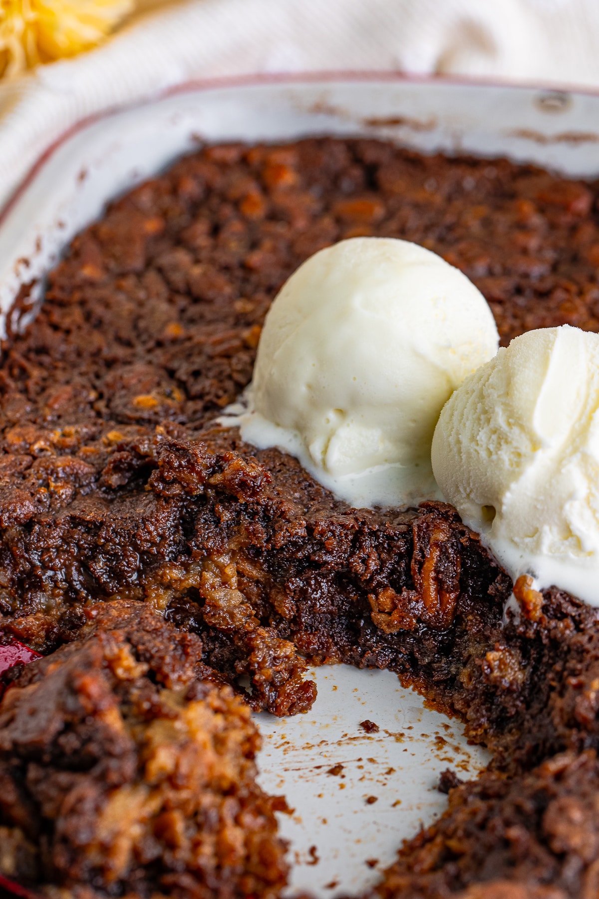 Pecan Cobbler in baking dish with ice cream on top, some of the dessert scooped out