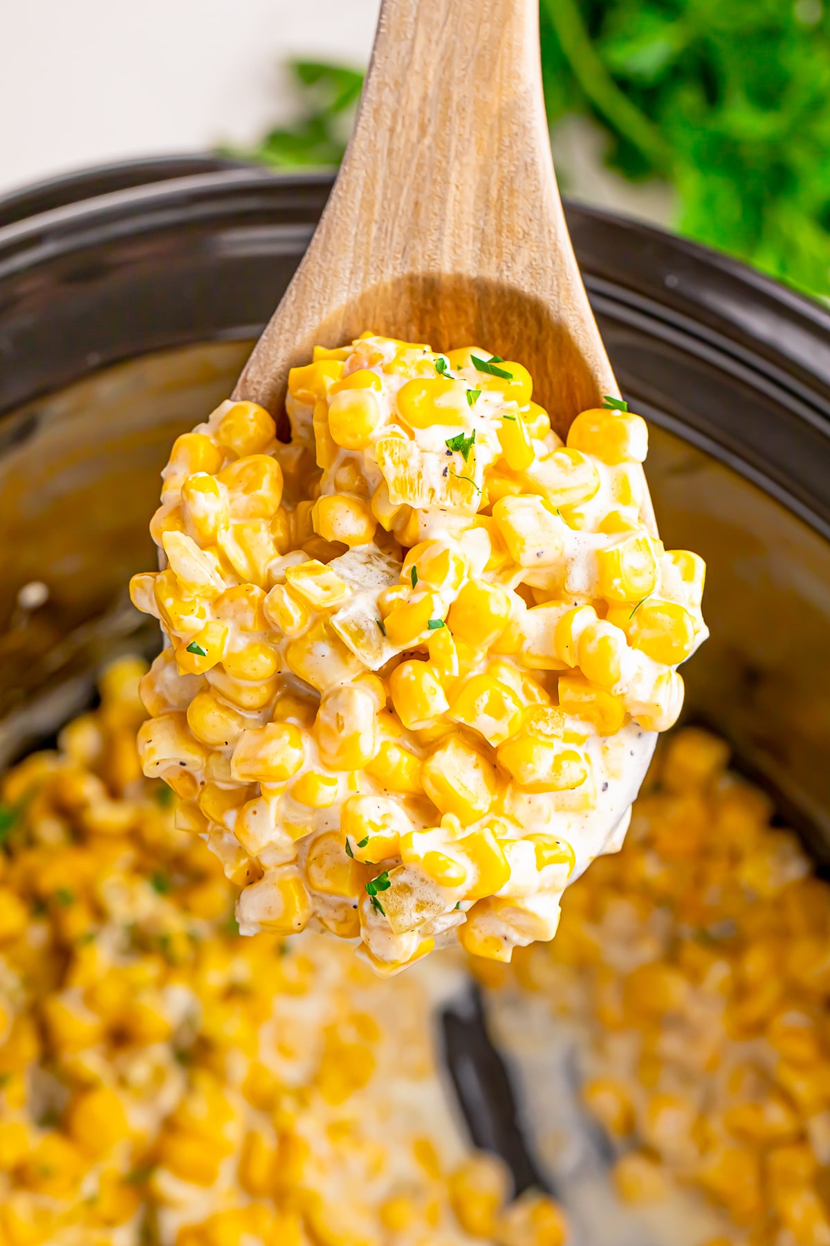 a spoon holding up a portion of Slow Cooker Creamed Corn in air