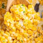 A wooden spoon lifting a scoop of creamy slow cooker creamed corn with green chiles over the crock.