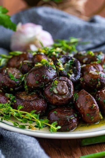 A plate of roasted mushrooms in garlic butter sauce topped with fresh herbs.