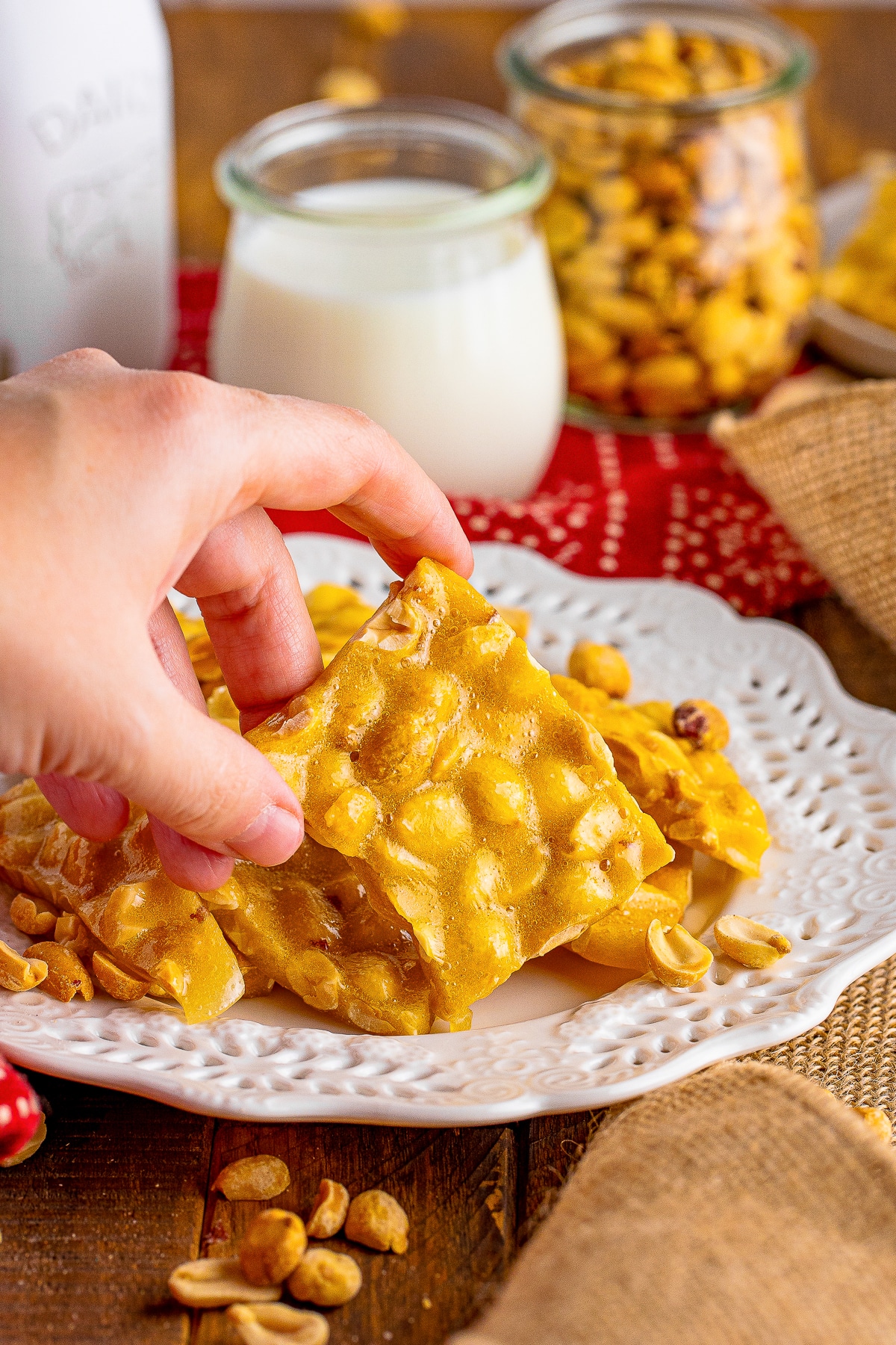 a hand grabbing a piece of Microwave Peanut Brittle off of serving plate