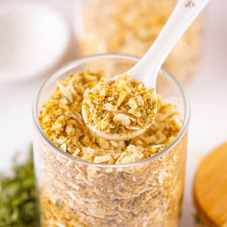 A spoon scooping Homemade Onion Soup Mix from a glass storage jar.